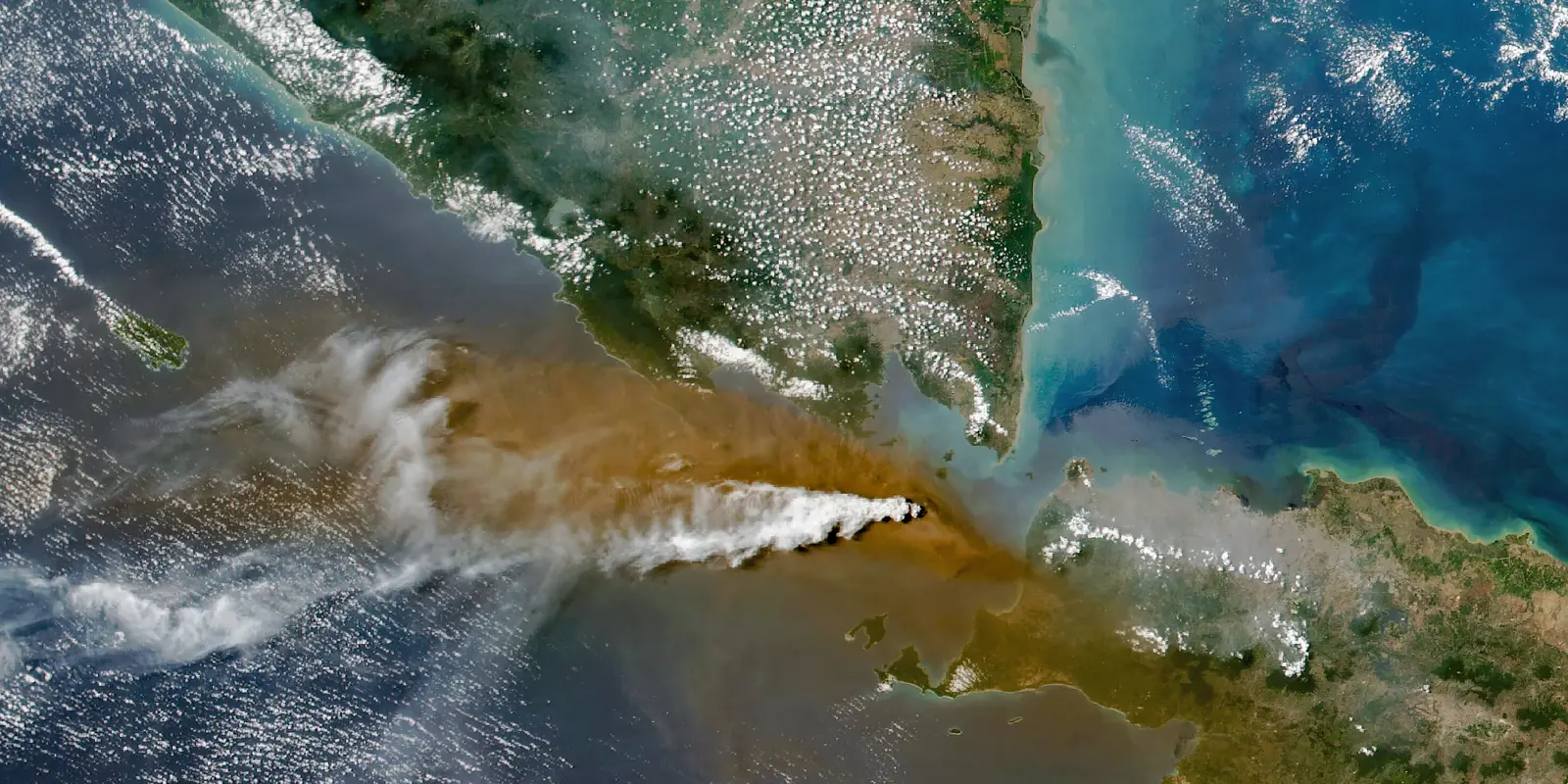 Citra satelit erupsi Anak Krakatau di Selat Sunda, dengan kolom abu cokelat yang menyebar ke timur melintasi laut ke arah Jawa dan Banten.